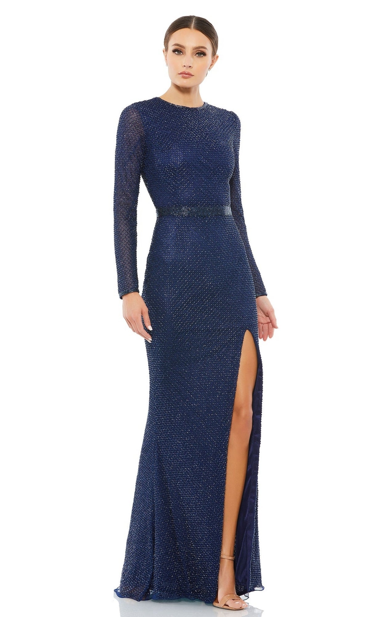 A woman stands against a plain white background wearing the Long Formal Dress 5056 by Mac Duggal—a dark blue, floor-length gown with long sleeves, a high slit, and subtle beading.